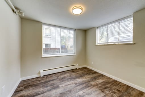 an empty living room with wood flooring and two windows