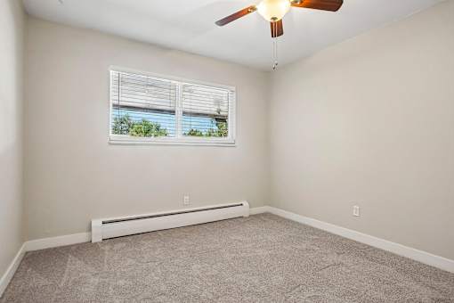 A room with a ceiling fan, carpeted floor, and a window with blinds.
