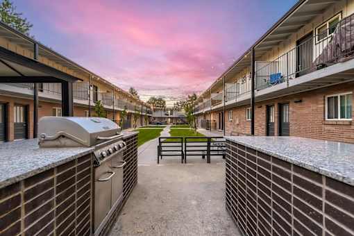 A sunset view of a courtyard with a BBQ grill and brick buildings.