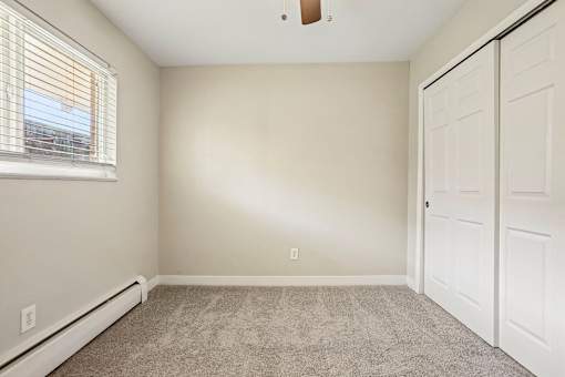A room with a carpeted floor, a window with blinds, and a white door.