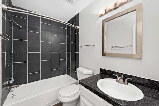 A bathroom with a black tiled shower area and a white toilet.