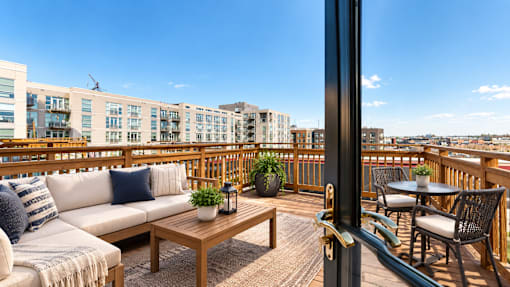A balcony with a white couch, a wooden table, and a view of a cityscape.
