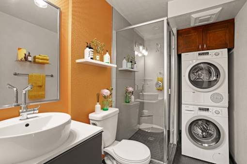 A modern bathroom with a white sink, toilet, and a washing machine in the doorway.