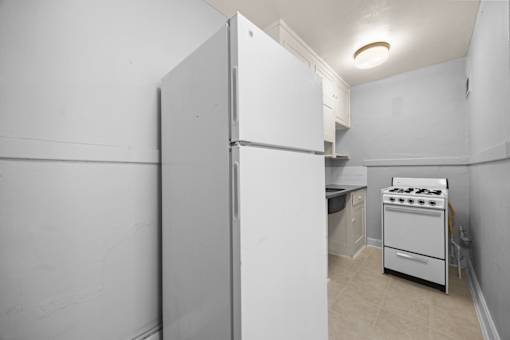 A white refrigerator stands in a kitchen with a stove and oven.