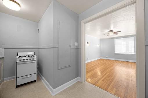 A kitchen with a stove and a wooden floor leading to a window.