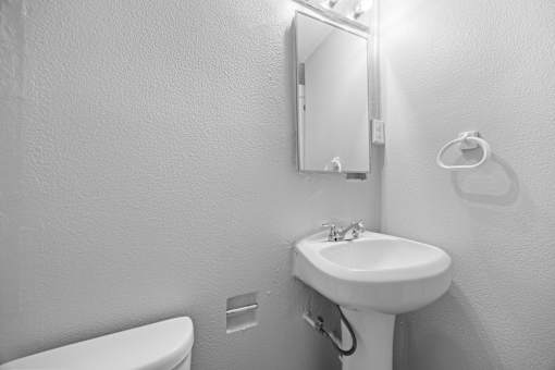 A bathroom with a toilet, sink, mirror and light.