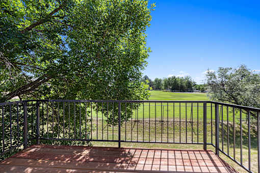 A balcony with a metal railing and a brick floor overlooks a grassy field.