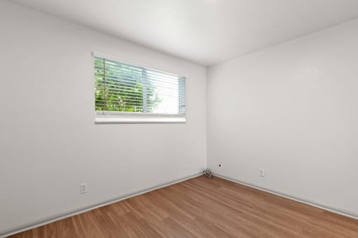 the living room of an empty house with a window and wooden floors