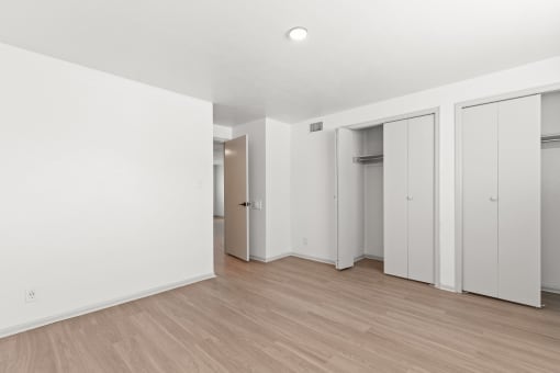 a bedroom with white walls and wood flooring and white closets