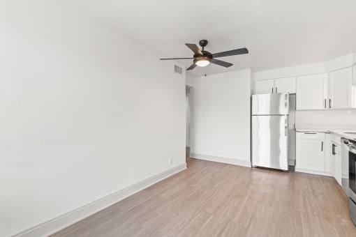 an empty living room with a ceiling fan and a refrigerator