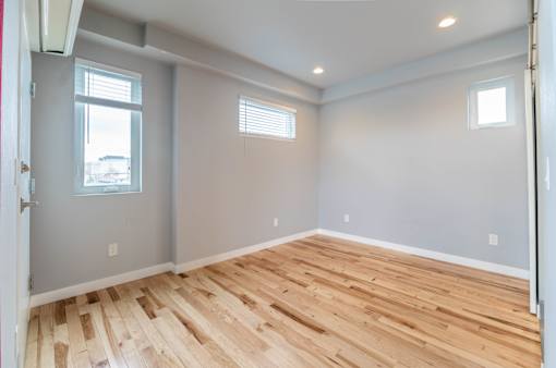 A room with wooden flooring and two windows.