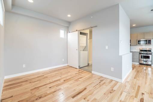 A room with wooden flooring and a kitchen area in the background.