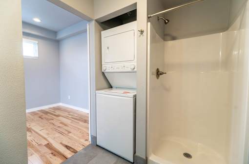 A white dishwasher is in a small bathroom with a walk-in shower.