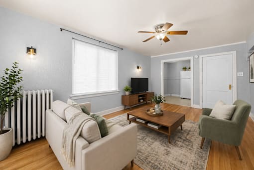 A living room with a beige couch, a green armchair, a wooden coffee table, and a ceiling fan.