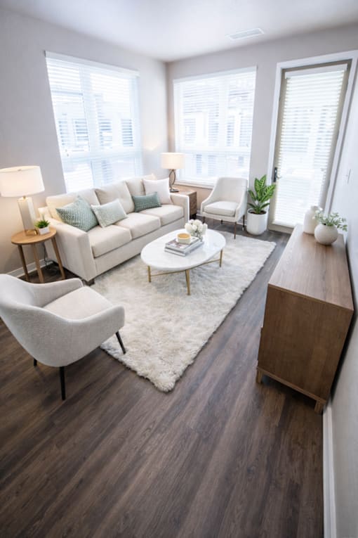 A modern living room with a white couch, a white rug, a wooden coffee table, and a white chair.
