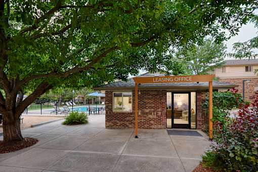 A leasing office is surrounded by greenery and has a pool in the background.
