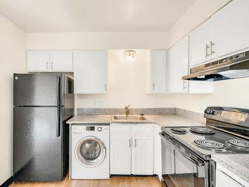 A black refrigerator sits next to a washing machine in a kitchen.