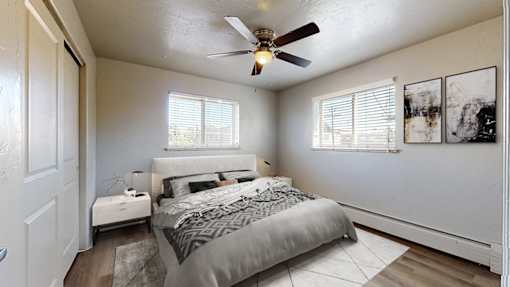 A bedroom with a bed, a ceiling fan, and a window with blinds.