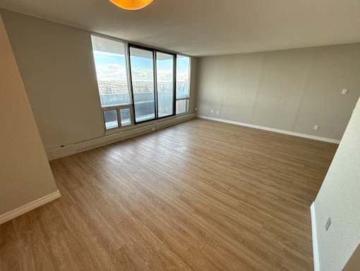 A room with wooden flooring and a large window overlooking a cityscape.