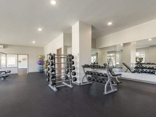 A spacious gym with a variety of equipment including dumbbells, weight plates, and a bench press.