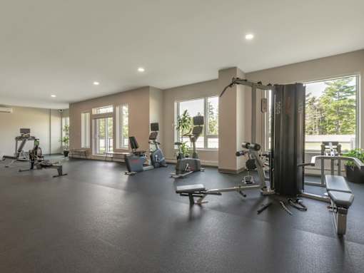 A spacious gym with various exercise equipment and a view of trees outside the windows.