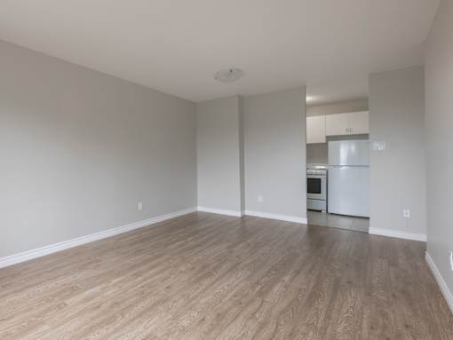 A spacious room with wooden flooring and a kitchen area in the background.