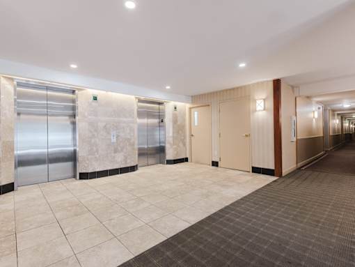 A hallway with a carpeted floor, tiled walls, and a row of elevators.