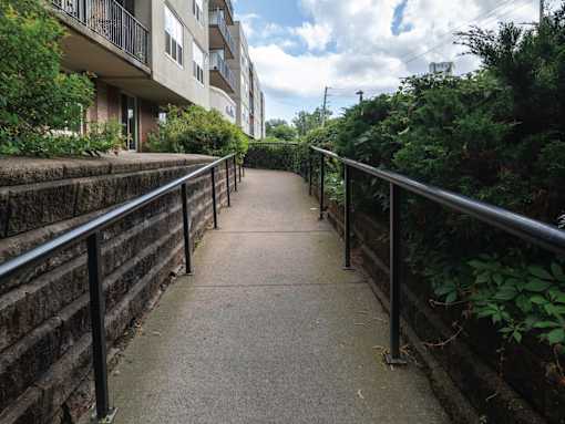 A concrete pathway with railings on both sides leads through a green area.