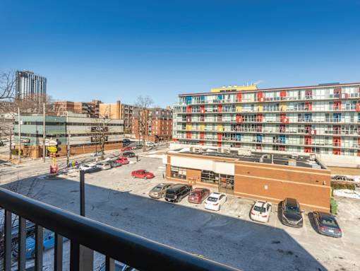 A parking lot with cars and a multi-story building with red and yellow balconies.