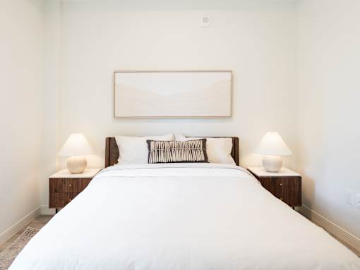 A bedroom with a large bed, two lamps, and a painting on the wall.
