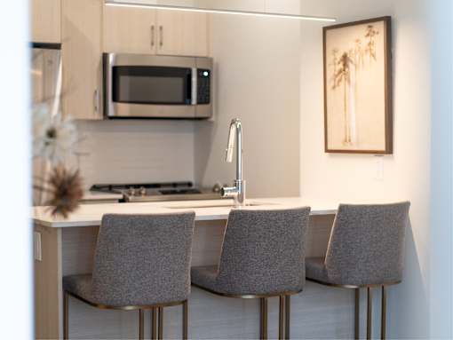 A modern kitchen with a white countertop and grey chairs.