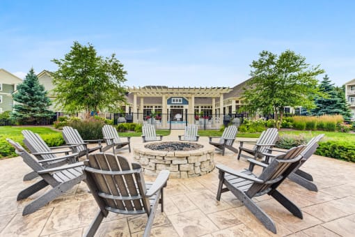 Luxury Apartments In Vernon Hills, IL - Outdoor Firepit Lounge Area With Wooden Chairs, and Lush Green Landscaping.