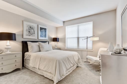 Apartments In Vernon Hills, IL For Rent - The Oaks of Vernon Hills - Spacious Bedroom With High Ceilings, Carpet Flooring, Bed, Nightstands With Lamps, Dresser, Floor Lamp, And Large Window With Blinds