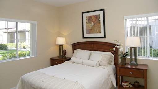A bedroom with a large bed, a nightstand with a lamp, and a framed picture on the wall.