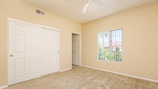 A room with a white door and a window with a view of trees and a house.