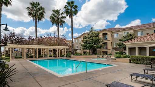 A pool surrounded by palm trees and a building in the background.