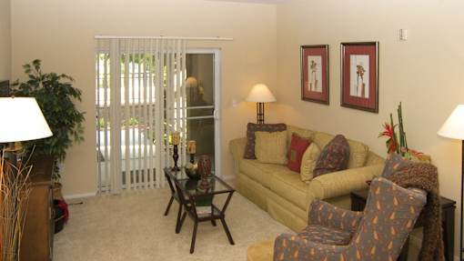 A living room with a yellow couch, a chair, and a table with a lamp.