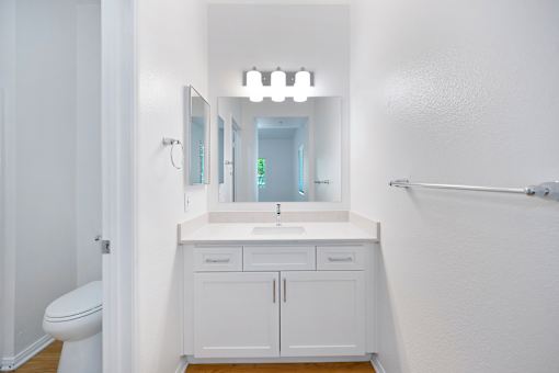 A white bathroom with a sink, mirror, and toilet.