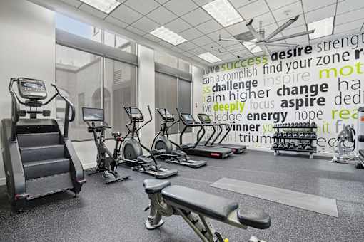 A gym with a variety of equipment and a motivational word cloud on the wall.