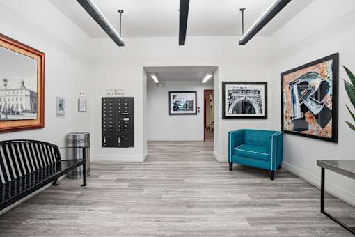 A room with a black bench, a blue chair, and a framed picture on the wall.