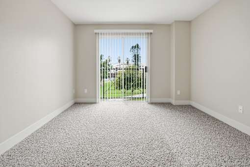 A room with a carpeted floor and a sliding glass door leading to a backyard.