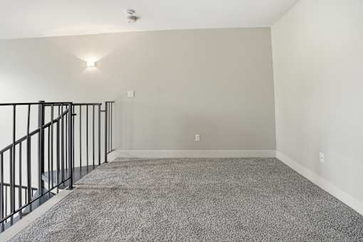 A spacious room with a carpeted floor and a staircase with black railings.