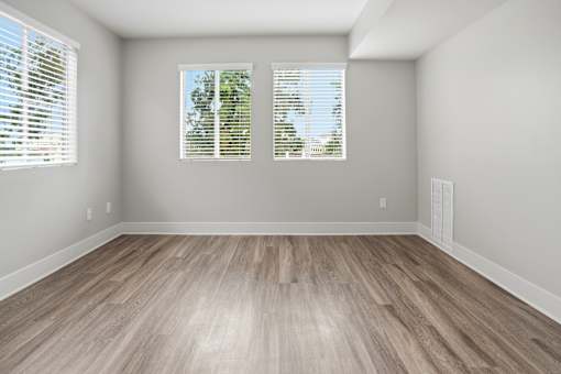 A room with wooden flooring and two windows with blinds.