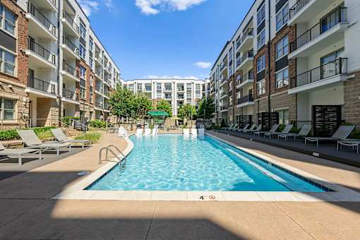 A swimming pool surrounded by lounge chairs and apartment buildings.