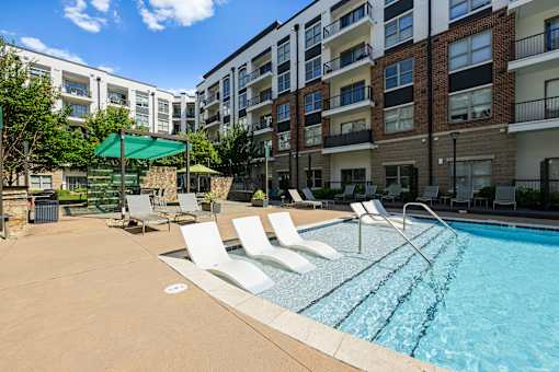 A swimming pool surrounded by lounge chairs and apartment buildings.
