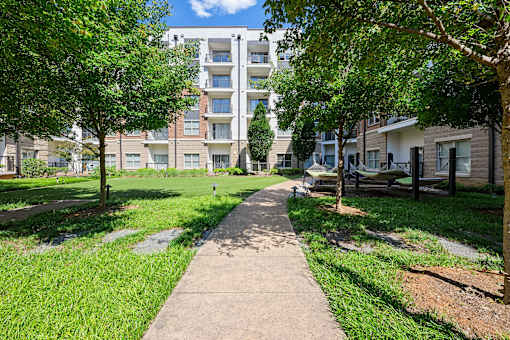 A walkway in a park with trees on either side and apartment buildings in the background.