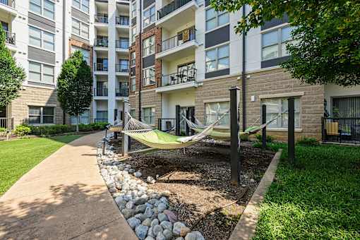 A hammock is strung between two poles in a grassy area in front of apartment buildings.