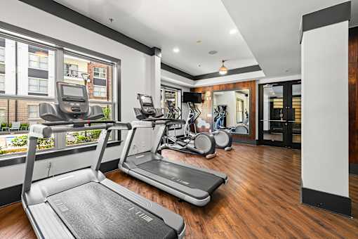 A treadmill in a gym with a view of a building outside the window.