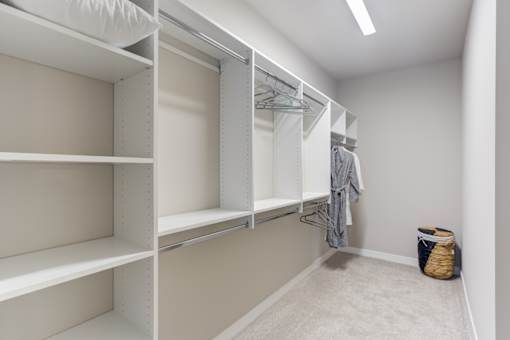 a walk in closet with white shelving and a basket on the floor