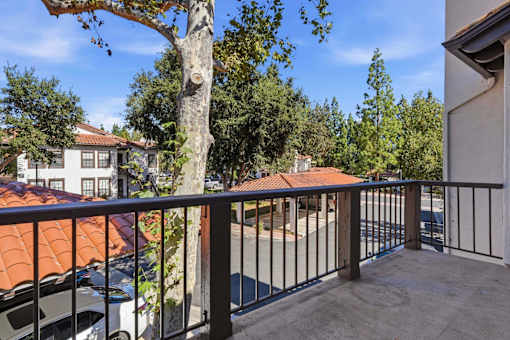 A balcony with a black railing and a tree in the foreground.